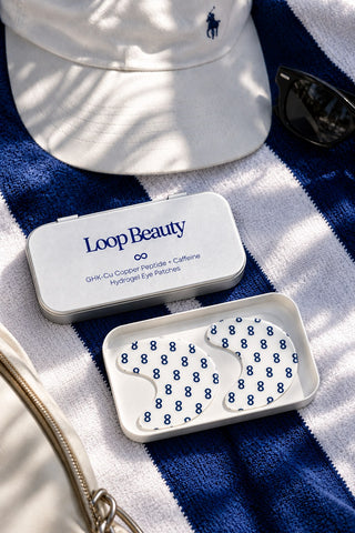Loop Beauty eye patches tin on striped beach towel with cap and sunglasses